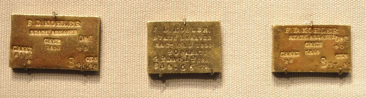 A row of small gold ingots from 1850, each stamped by the California State Assay Office with its weight and fineness.