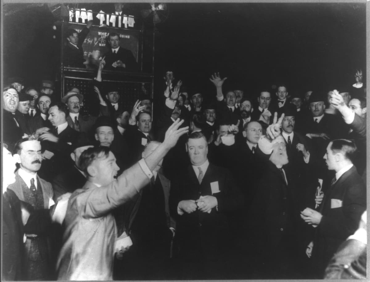 Traders packed into the wheat pit of the Chicago Board of Trade in 1920, arms raised, signalling bids with their hands and shouting.