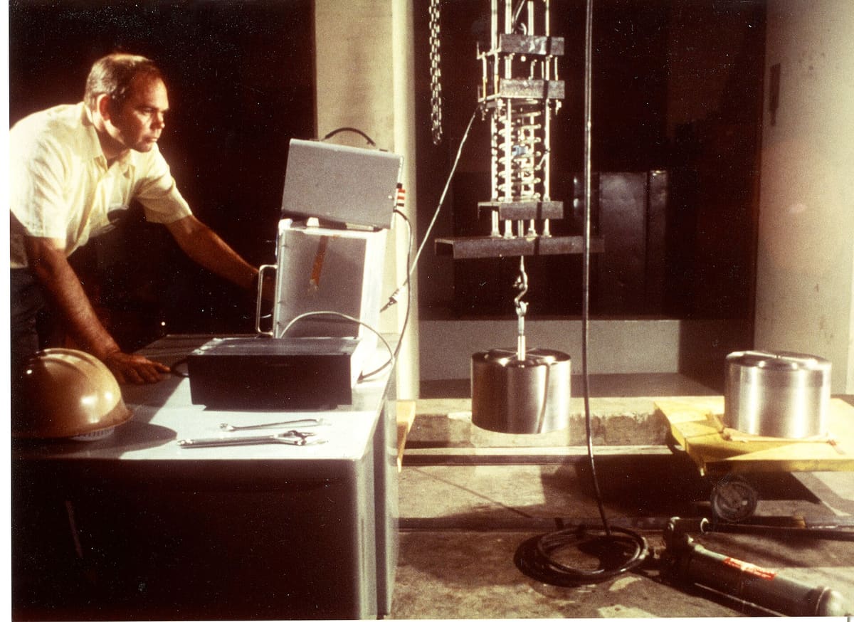 An engineer at a control desk weighing a 500-pound stainless steel standard hung from a load cell comparator.