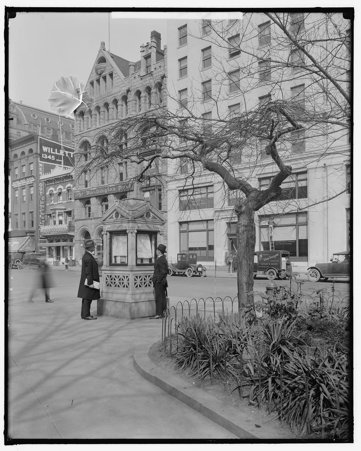 Two men in hats read the day's posted weather map at a U.S. Weather Bureau kiosk on a Washington street corner.
